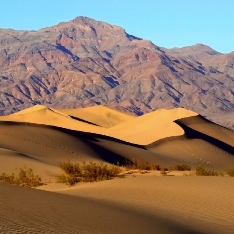 Sanddünen im Vordergrund vor einem Gebirge unter blauem Himmel