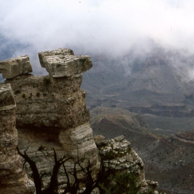Aussicht von einer Felsformation auf ein nebelverhangenes Gebirge mit Menschen auf dem Kantenbereich.
