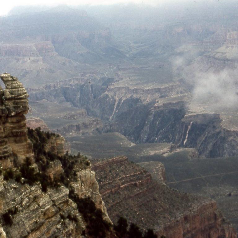 Weitwinkelaufnahme eines tiefen Canyon-Systems mit sichtbaren geologischen Schichten und Nebel.