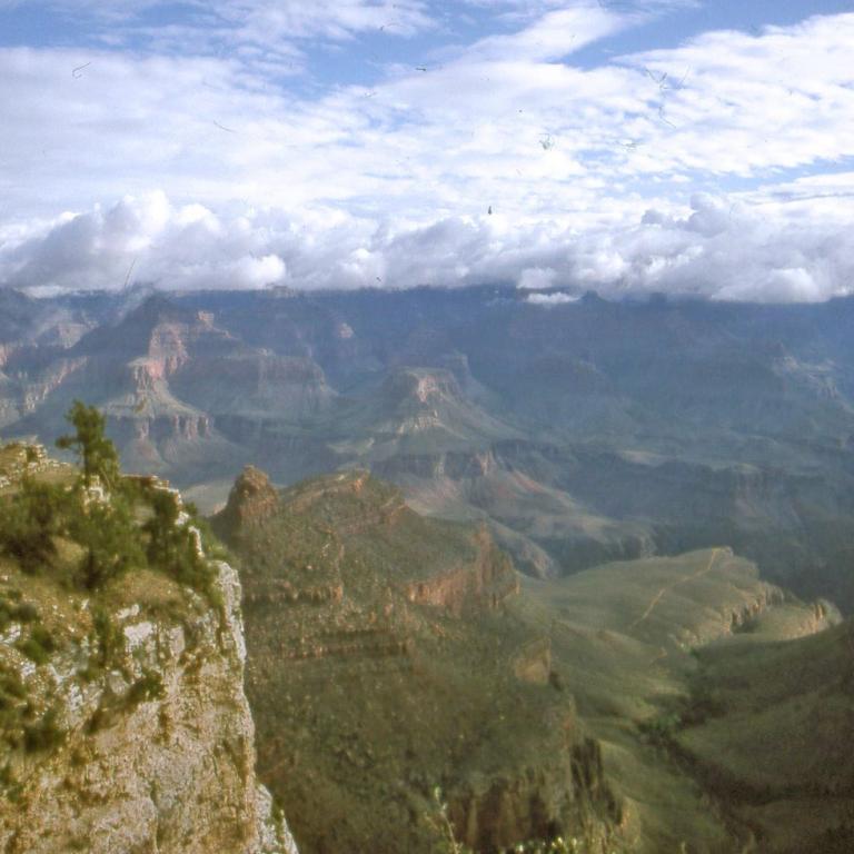 Weitläufiger Panoramablick von Klippen auf tiefe Täler und Bergketten unter einer Wolkendecke.