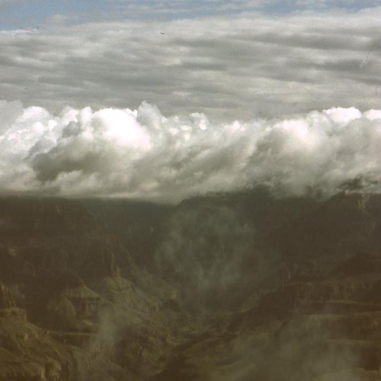 Luftaufnahme einer Berglandschaft, die von dicken Wolken und Nebel umhüllt ist.