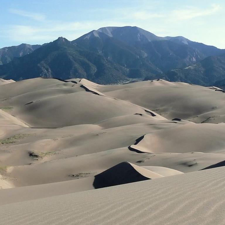 Eine weite Landschaft mit sanften Sanddünen im Vordergrund und einer großen Bergkette im Hintergrund.