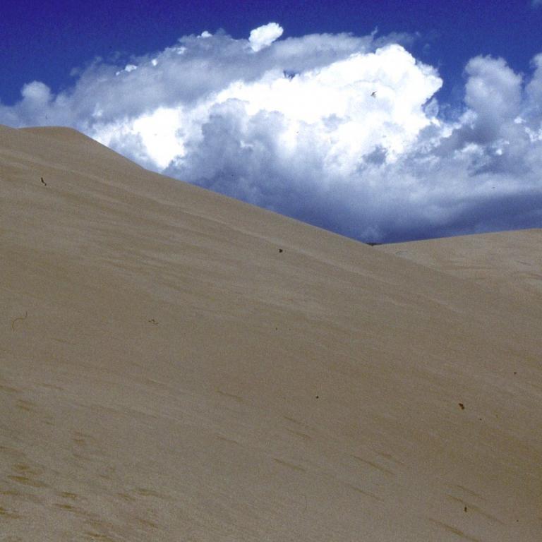 Eine große, sanfte Sanddüne unter einem blauen Himmel mit weißen Wolken.