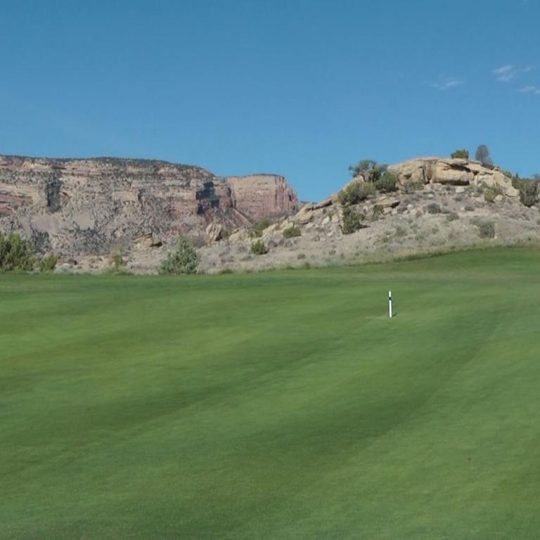 Ein Golfplatz mit grüner Wiese im Vordergrund vor der Kulisse dramatischer roter Klippen.