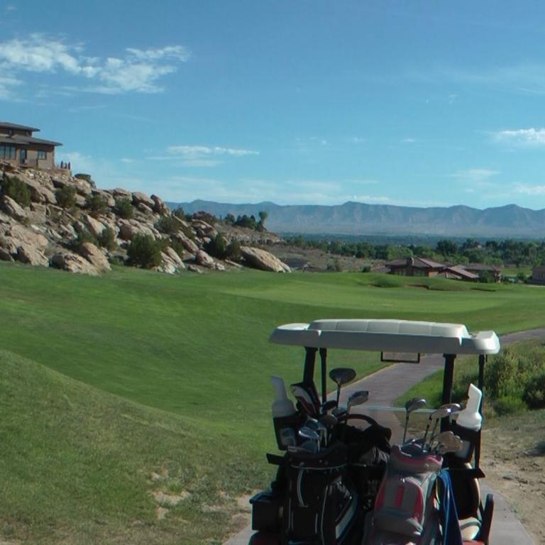 Panoramablick auf einen Golfplatz mit einem Haus auf einer felsigen Klippe im Hintergrund.