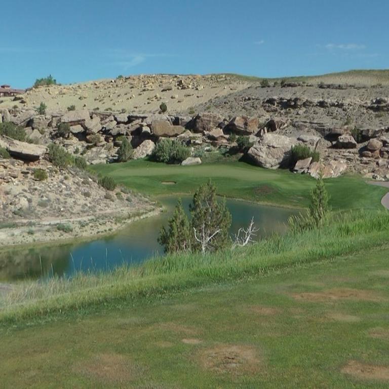 Weitwinkelaufnahme eines Golfplatzes mit einem Teich, umgeben von felsigem, hügeligem Gelände.