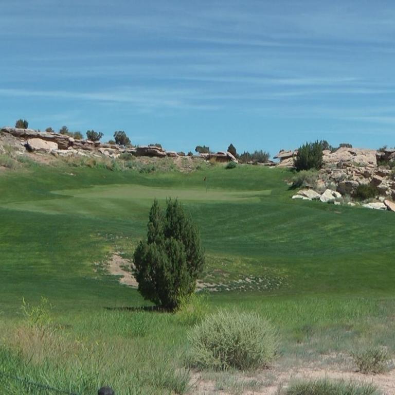 Grüner Golfplatz mit Blick auf felsiges Gelände und blauen Himmel