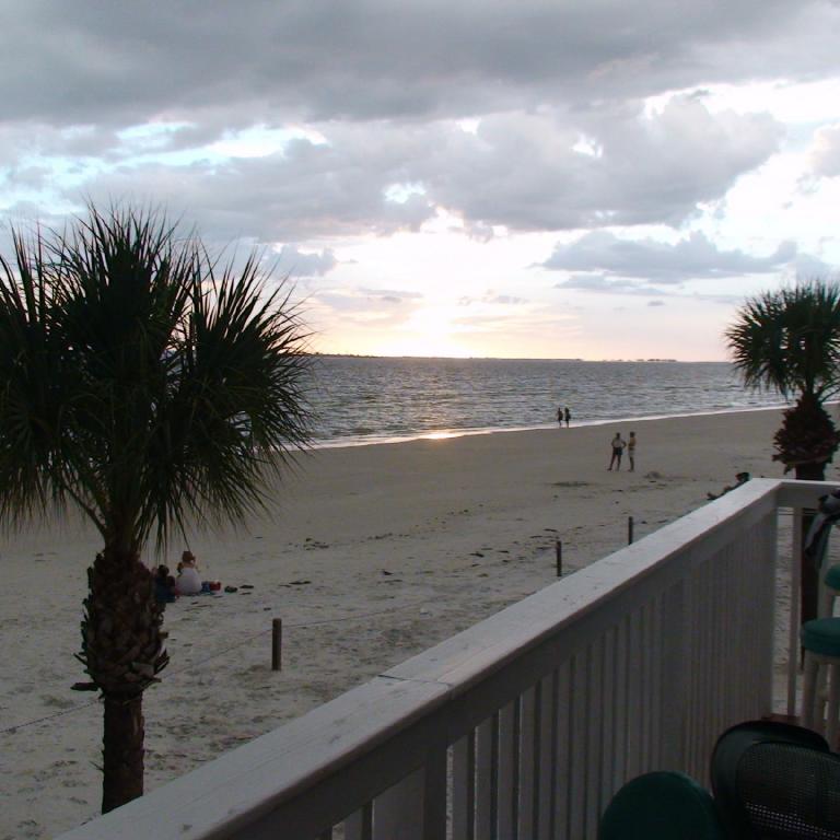 Blick auf einen Strand bei Sonnenuntergang von einem Balkon aus, mit Palmen und Blick aufs Meer.