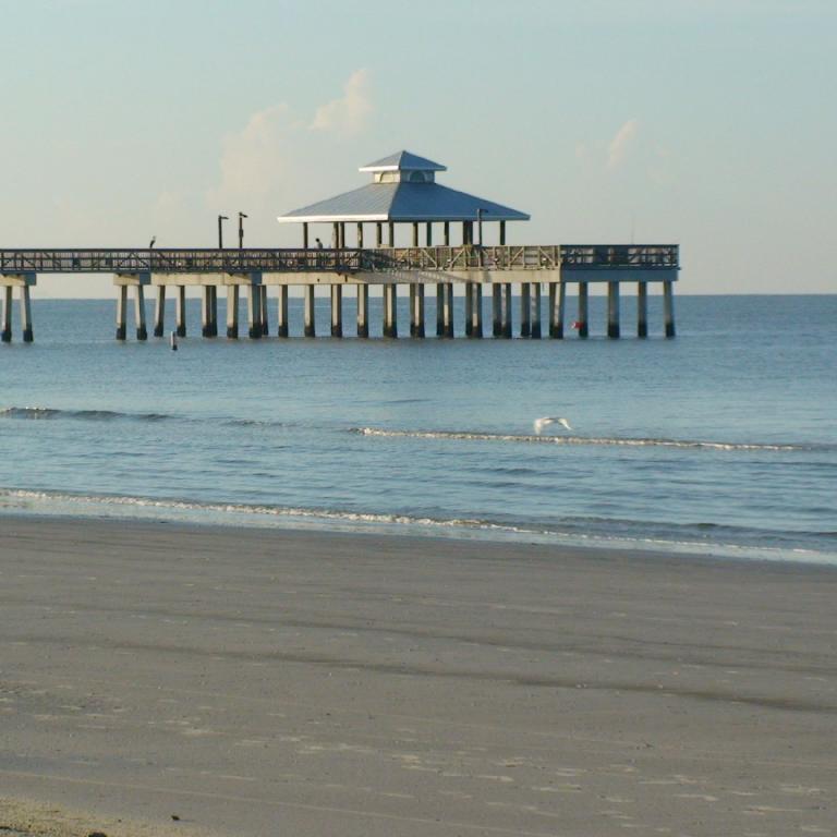 Ein Holzpier ragt über das Meer aus, der von einer sandigen Bucht umgeben ist.