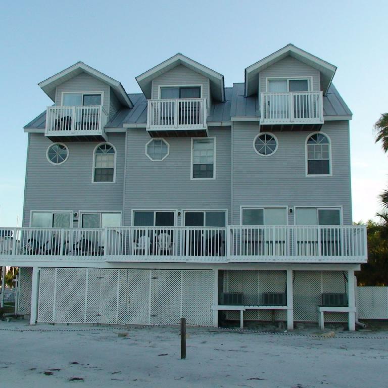 Ein großes, modernes zweistöckiges Wohnhaus mit mehreren Balkonen und Gauben, das direkt an einem breiten Sandstrand steht.