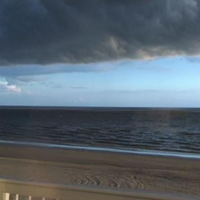 Dramatische Aufnahme vom Meer unter einem schweren Wolkenhimmel mit Sandstrand und Geländer im Vordergrund