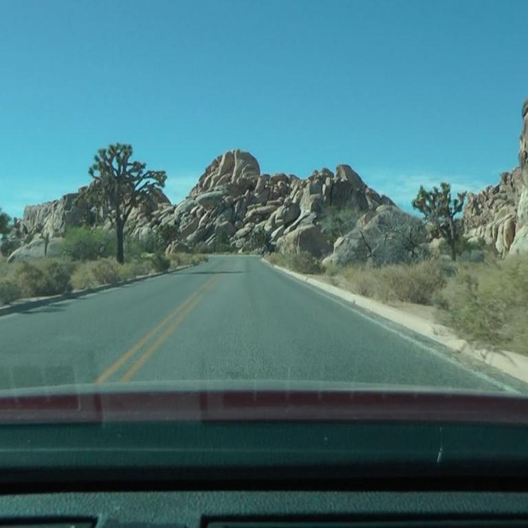 Blick auf eine Straße durch eine felsige Wüstenlandschaft von einem Fahrzeug aus.