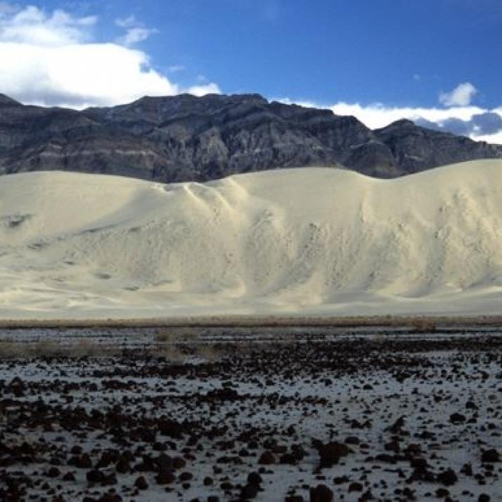 Weite Sanddünen vor einem Bergpanorama unter blauem Himmel