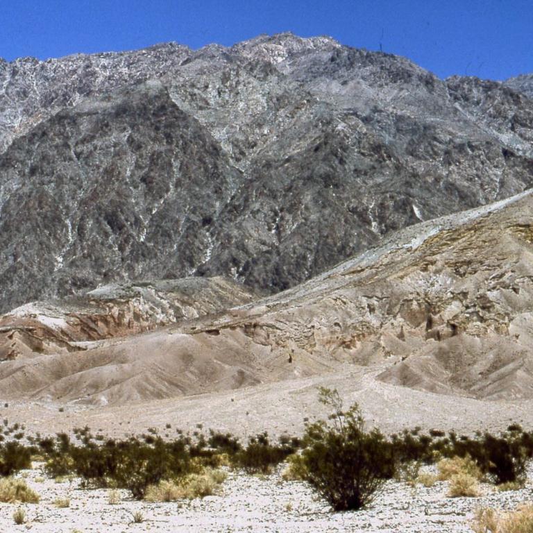 Weite Aufnahme einer trockenen, bergigen Landschaft mit Buschwerk und felsigen Gipfeln.