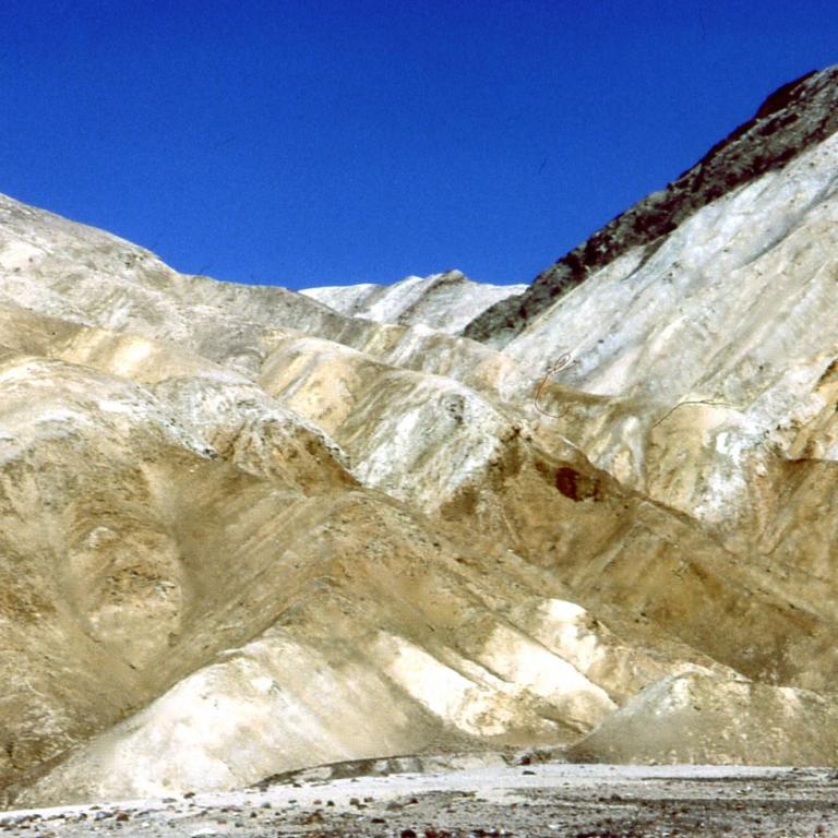 Geologische Formation mit hellen, terrassenartigen Hängen unter einem klaren blauen Himmel.