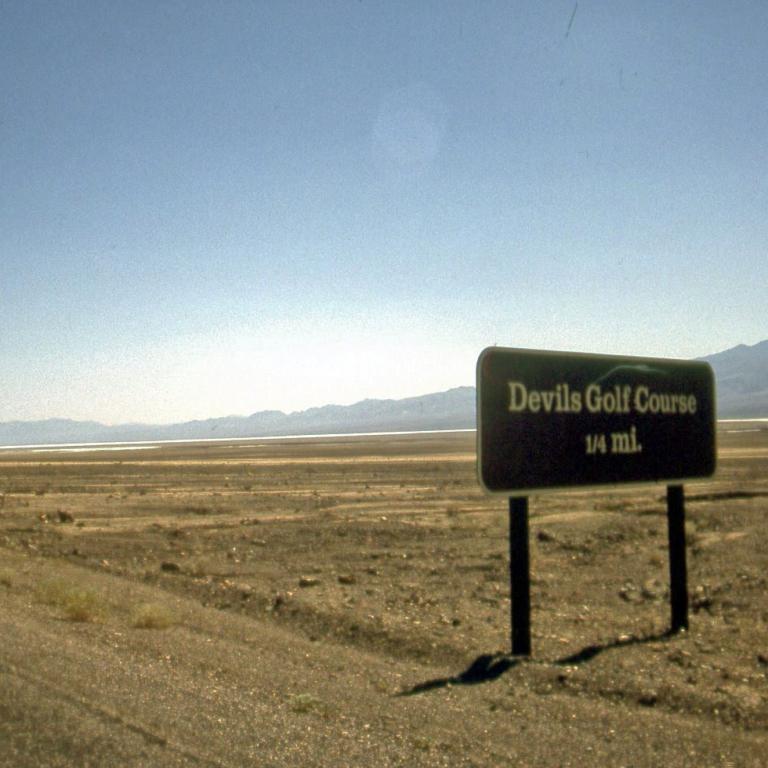 Ein Wegweiser für einen Golfplatz namens Devils Golf Course, platziert in einer trockenen Wüstenlandschaft.