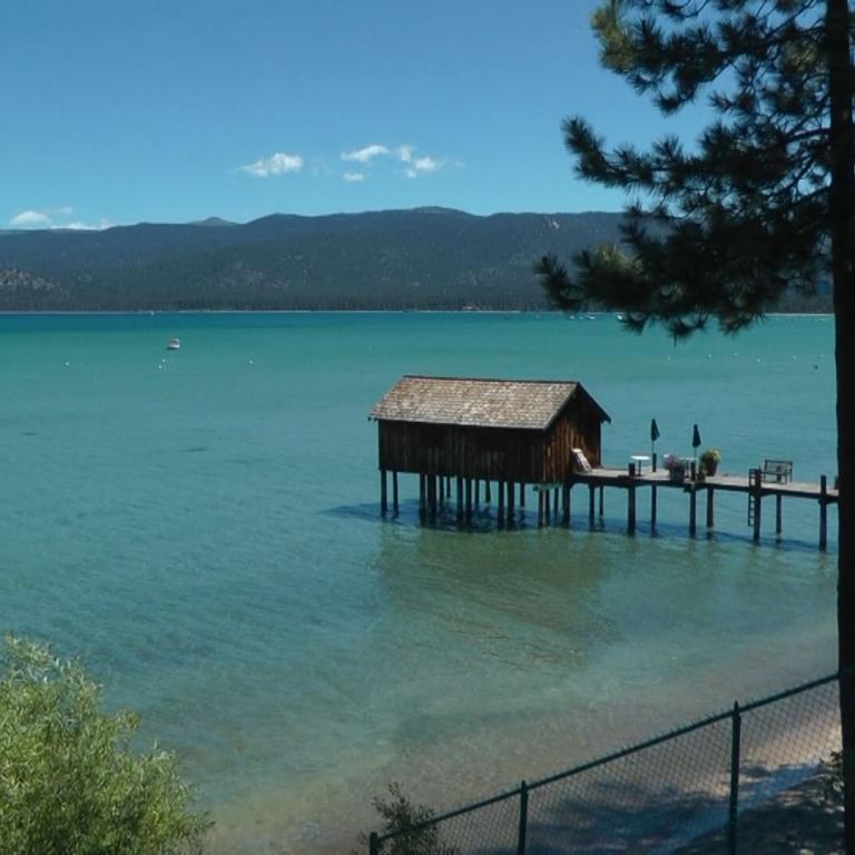 Panoramablick auf einen großen See mit einem Holzhaus auf Stelzen und bergigem Hintergrund