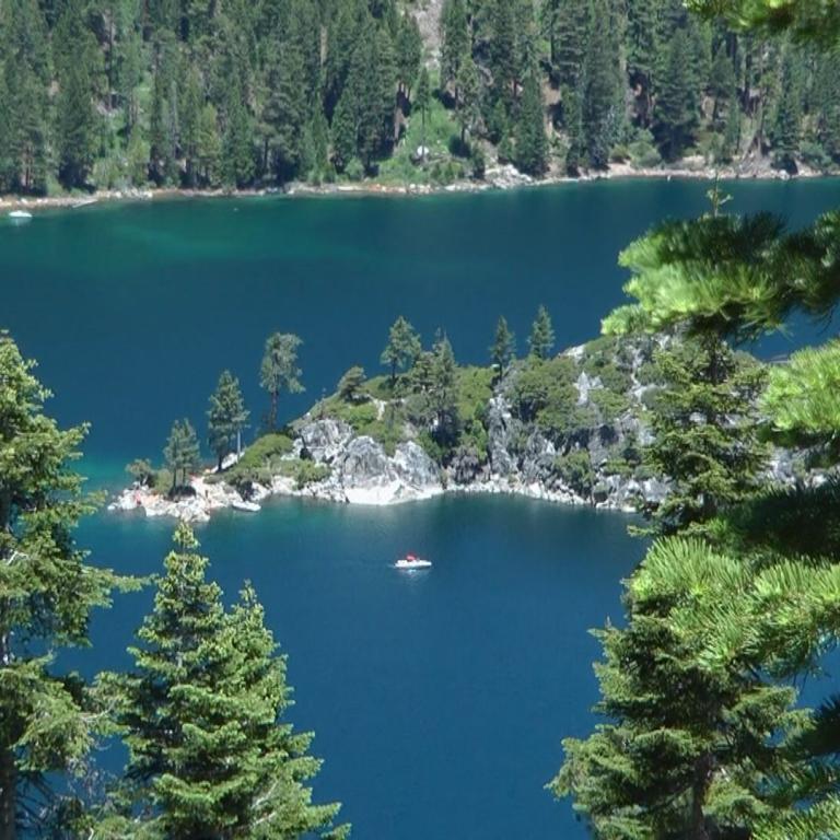 Panoramablick auf einen tiefblauen Bergsee, umrahmt von dichten Nadelwäldern im Vordergrund und Hintergrund.