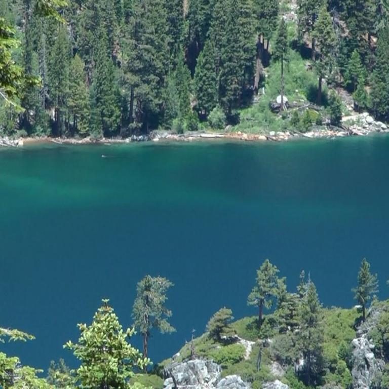 Ein tiefblauer Bergsee, umgeben von einem dichten Nadelwald und steilen Berghängen.