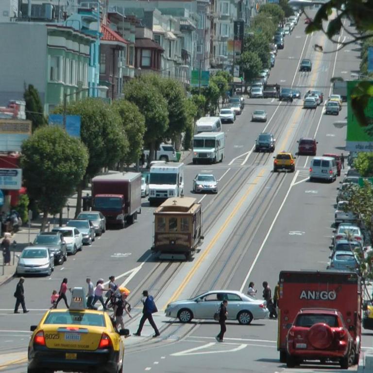 Ein Blick auf eine breite, belebte Hauptstraße durch ein städtisches Viertel mit Verkehr und Gebäuden.