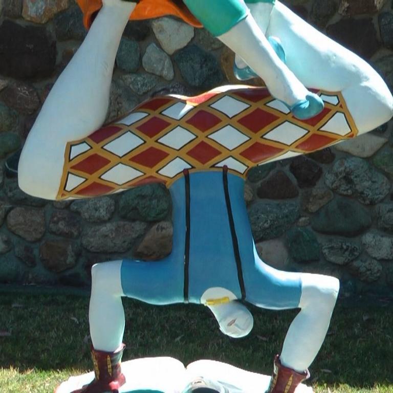 Eine überdimensionale Statue einer Person in einer akrobatischen Pose vor einer Natursteinmauer.