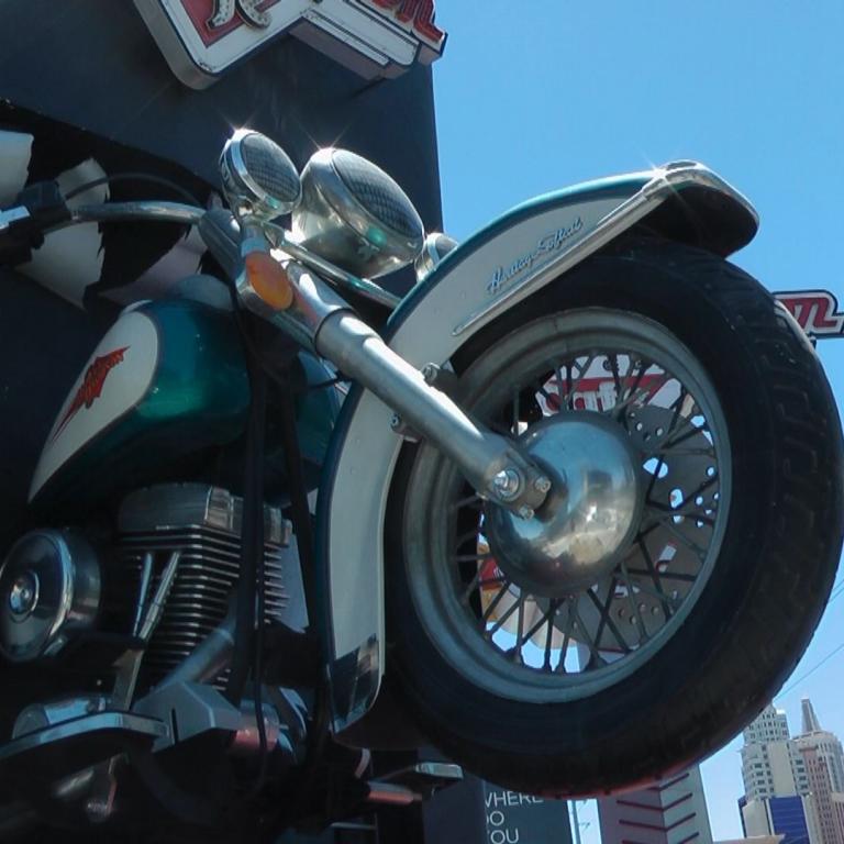 Ein klassisches, chromverziertes Motorrad steht vor einer modernen Skyline aus Glasgebäuden.
