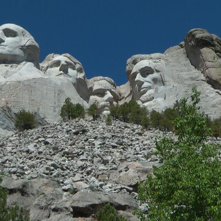 Gruppe von Skulpturen von Gesichtern in Felsformationen unter blauem Himmel