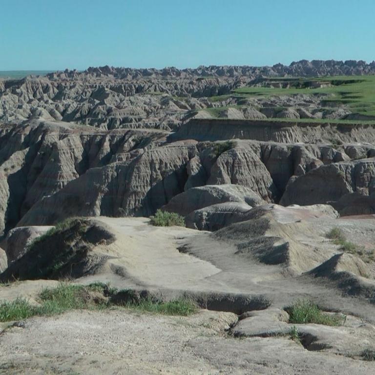 Eine weite, zerklüftete Landschaft mit erodierten Felsformationen und einer flachen grünen Ebene im Hintergrund.