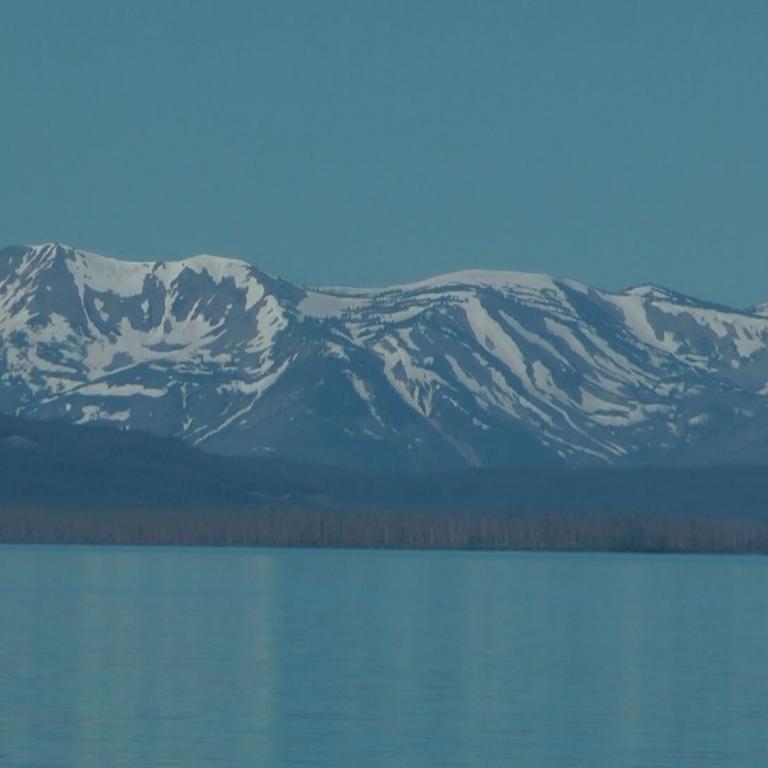 Eine schneebedeckte Bergkette am Ufer eines großen Sees unter klarem blauem Himmel.