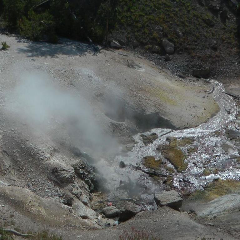 Geothermische Senke mit aufsteigendem Dampf zwischen steilen, bewachsenen Hängen.
