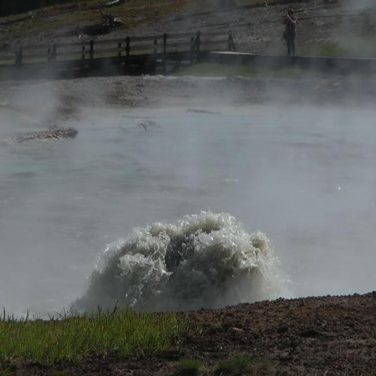 Ein Wasserfall stürzt über ein dunkles Flussbett, wodurch viel Gischt entsteht.