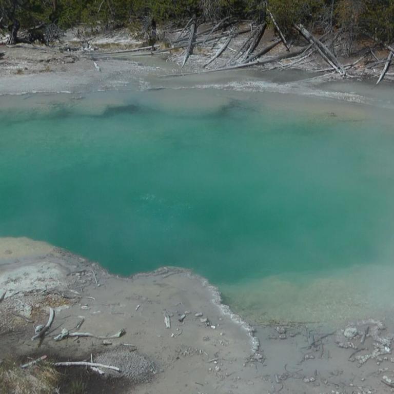 Ein großer, türkisfarbener Mineral- oder Geothermalsee in einer kargen, natürlichen Umgebung.