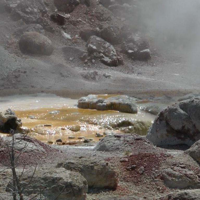 Geothermische Szene mit Dampf, mineralreichem Wasserbecken und großen Felsformationen