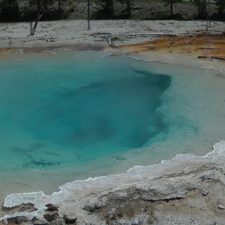 Ein türkisfarbenes Thermalbecken, umgeben von weißen Mineralablagerungen und trockenem Boden.
