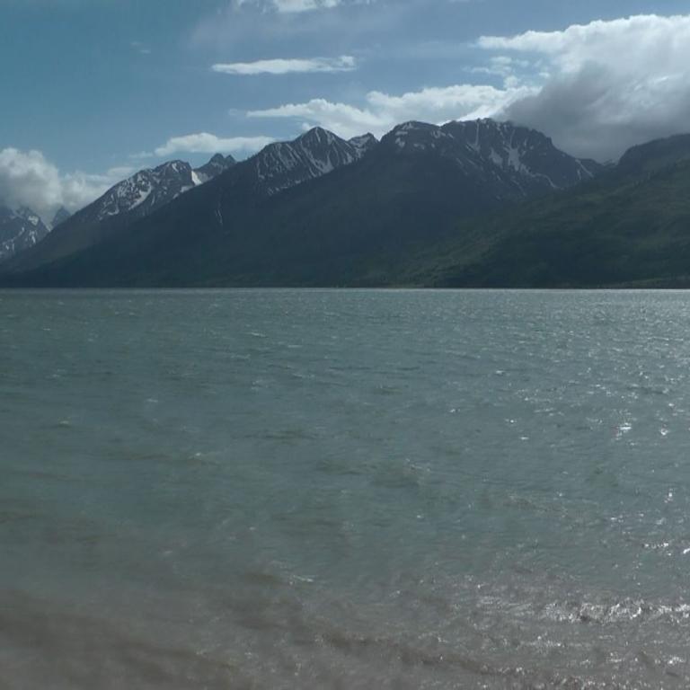 Panorama mit Wasserfläche und schneebedeckten Bergen unter dramatischem Himmel.