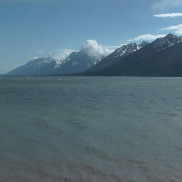 Eine weite Wasserfläche vor einer majestätischen Bergkette, die unter einem bewölkten Himmel aufragt.