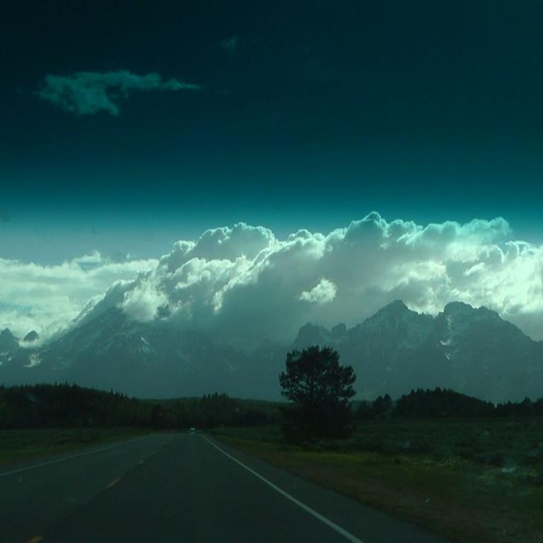 Eine Panoramaansicht einer Straße vor einer beeindruckenden Bergkette hinter einem Wolkenmeer.