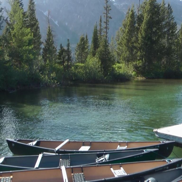 Ein ruhiger Bergsee mit mehreren Kanus im Vordergrund und dichten Wäldern an den Ufern.