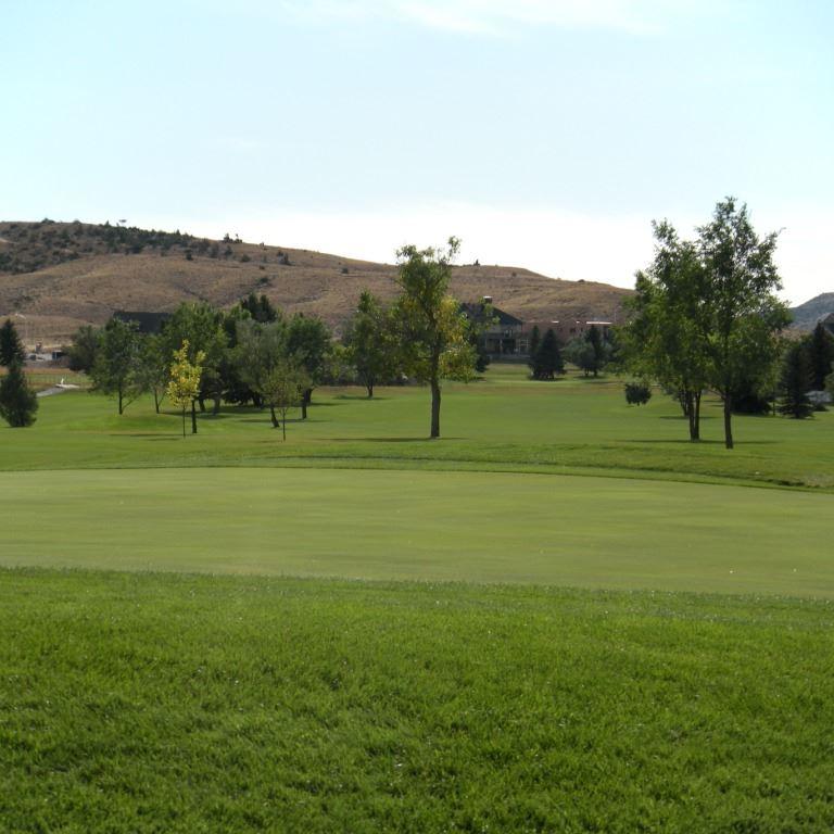 Panoramablick auf ein Golfplatzgelände mit sanften Hügeln und Bäumen im Hintergrund.