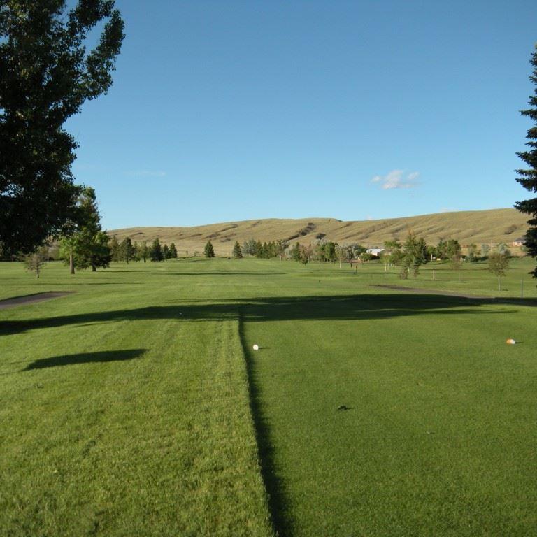 Große Bäume rahmen eine weite Aussicht auf einen gepflegten Golfplatz mit sanften Hügeln ein.