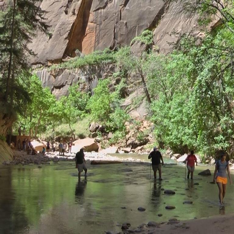 Eine Gruppe von Menschen steht am Ufer eines ruhigen Flusses in einem tief eingeschnittenen, bewaldeten Canyon.
