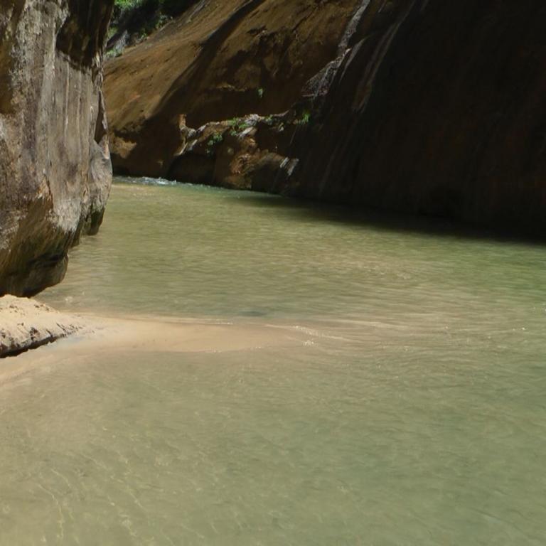 Blick in eine tiefe Schlucht mit steilen Felswänden und einem grünbraunen Fluss