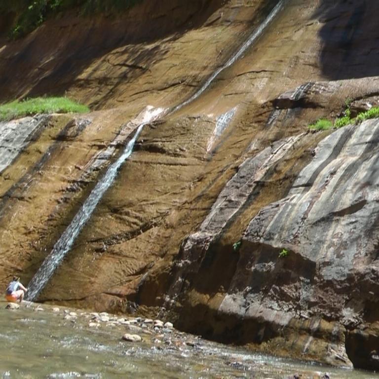 Eine Kaskade fließt über eine geologisch geschichtete Felswand an einem Fluss.