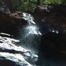 Ein kleiner Wasserfall stürzt über dunkle, nasse Felsformationen in einer natürlichen Umgebung.