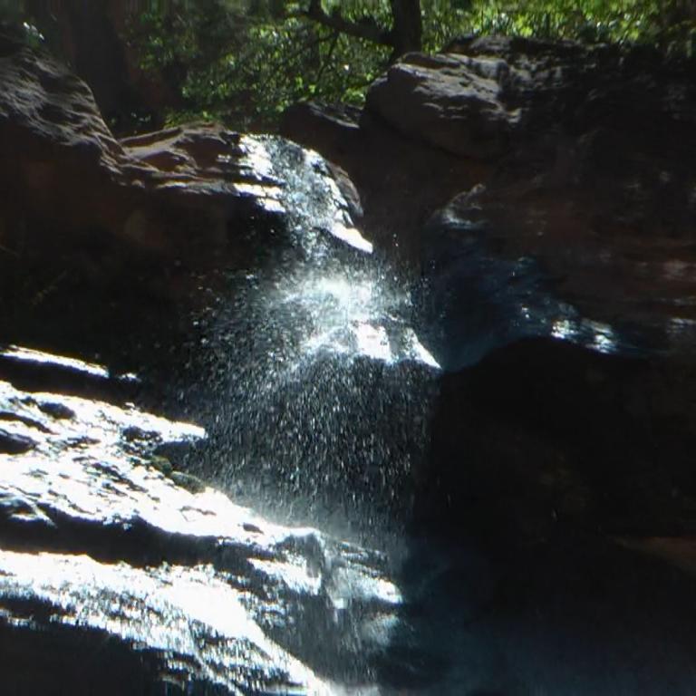 Ein kleiner Wasserfall stürzt über dunkle, nasse Felsformationen in einer natürlichen Umgebung.