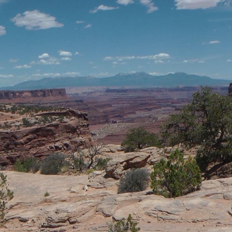 Weite Landschaftsaufnahme von Canyons und mesas mit felsigem Vordergrund.