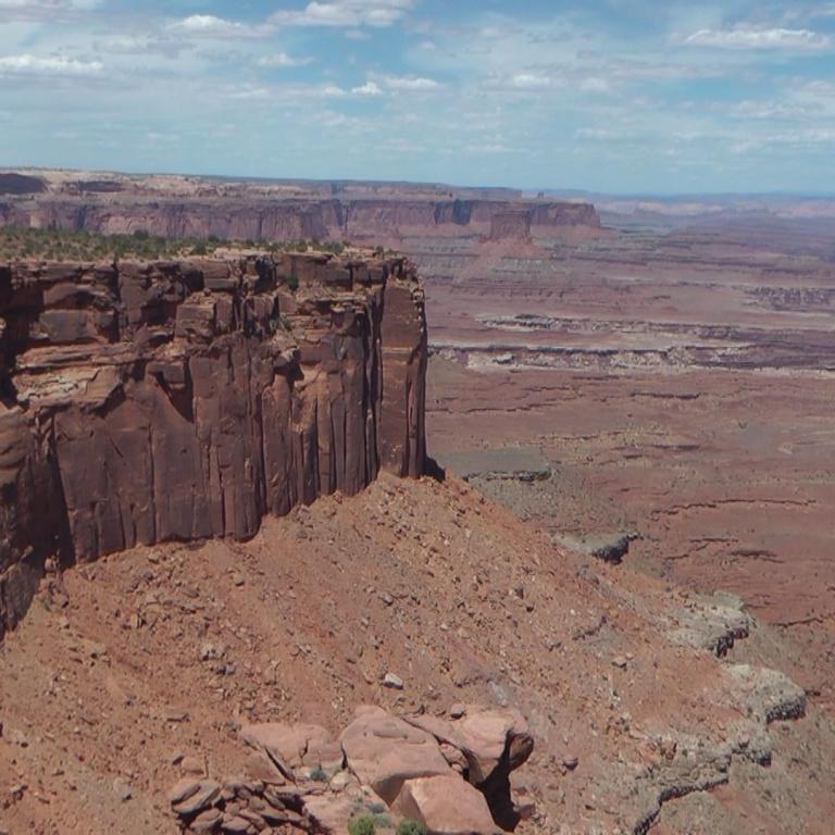 Panoramaansicht eines steilen Felsplateaus, das über eine weite, aride Canyonlandschaft blickt.