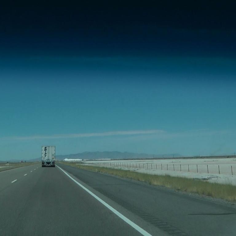 Blick auf eine weitläufige, gerade Autobahn, die durch eine offene Landschaft unter blauem Himmel führt.