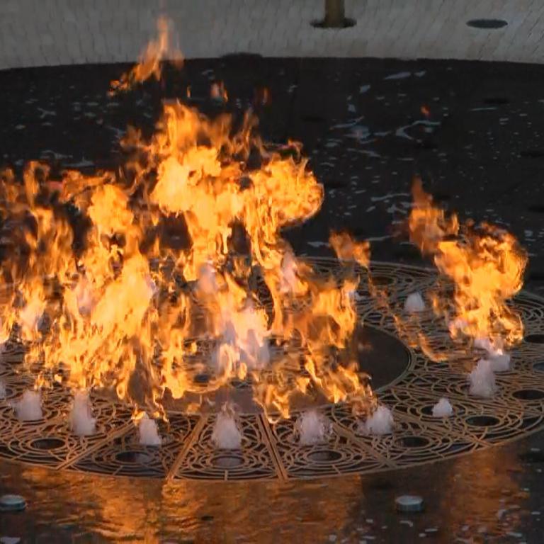 Ein großes, hell brennendes Feuer in einem runden Metallgitter auf nassem Boden.
