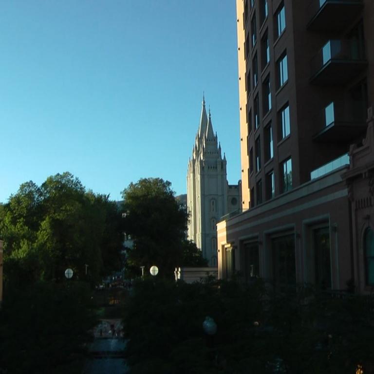 Panoramaaufnahme von mehreren modernen Gebäuden und einer historischen Kirche unter blauem Himmel.